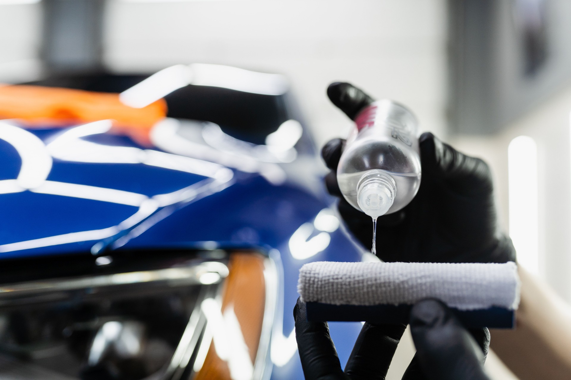 Detailing service, detailer worker applies ceramic protective liquid on sponge close-up. Process of pouring ceramic liquid from bottle on sponge to apply protective coating on car.