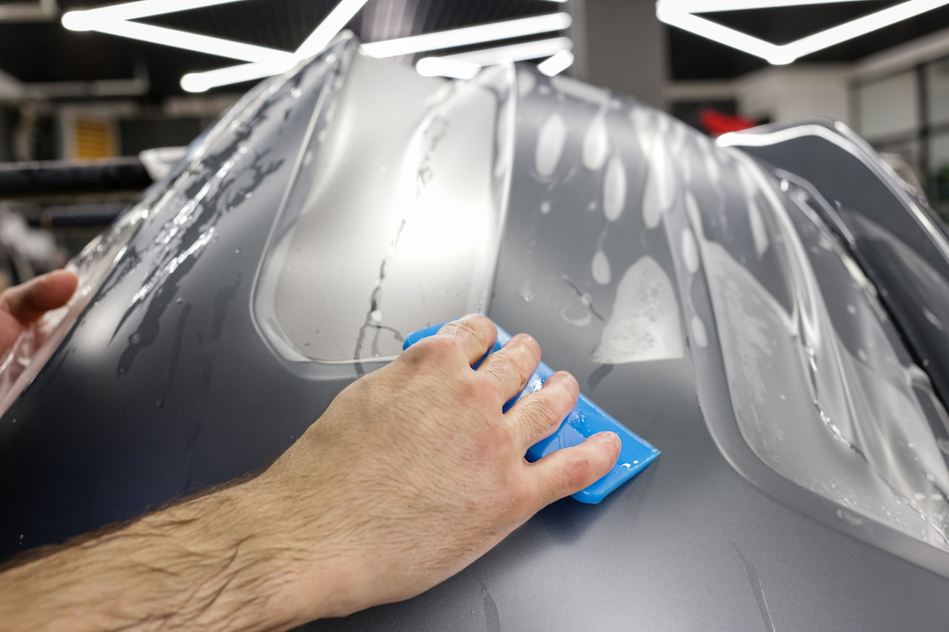 Close up of paint protection film installation on front bumper of modern luxury car. PPF is polyurethane film applied to car surface to protect the paint from stone chips, bug splatter, and abrasion.